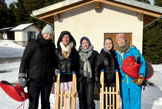 Fünf Schülerinnen mit Schlitten stehen vor einem Haus im Schnee